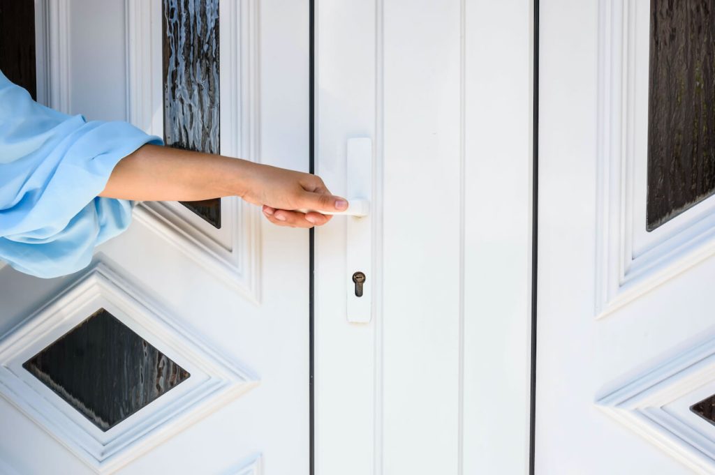 Close-up of a white uPVC front door with diamond-shaped glazed panels, as a person in a blue sleeve reaches for the handle.