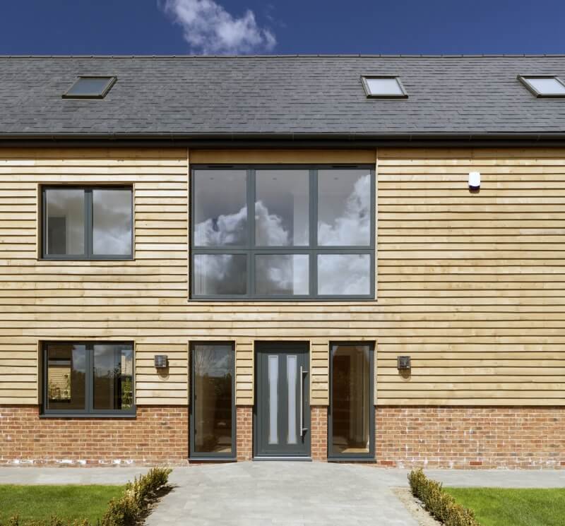 Contemporary home with Smarts Alitherm aluminium windows in a sleek grey finish, set against timber cladding and brickwork for a modern contrast.