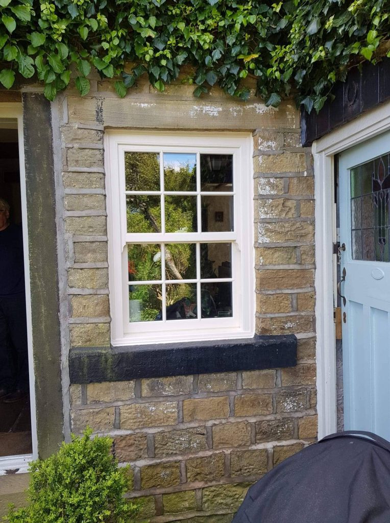 Sliding sash window with a white frame set in a stone cottage wall, surrounded by ivy.